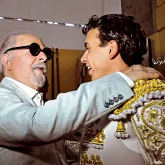 Un hombre mayor con gafas de sol abraza al torero Juan de Castilla, quien luce su traje de luces.