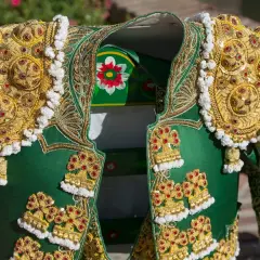 Detalle de un traje de luces de torero, con bordados dorados y pedrería roja sobre tela verde.