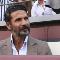 Un torero y actor español, con barba canosa y mirada intensa, viste chaqueta de lino y camisa a rayas.