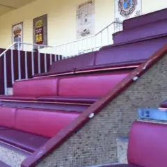 Asientos de terciopelo rojo en un palco de las ventas, con escaleras y barandillas blancas.