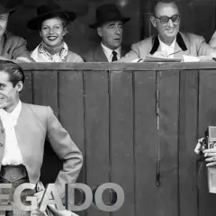 Un torero posa sonriente, mientras un fotógrafo captura el momento. Detrás, un grupo de espectadores, evocando la época de los toreros de los 90.