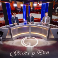 Tres hombres sentados en un plató de televisión con el logo "Grana y Oro" en el fondo y en el suelo.