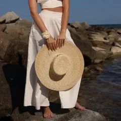 Mujer con un sombrero para ir a los toros, vestida de blanco, de pie sobre rocas junto al mar.