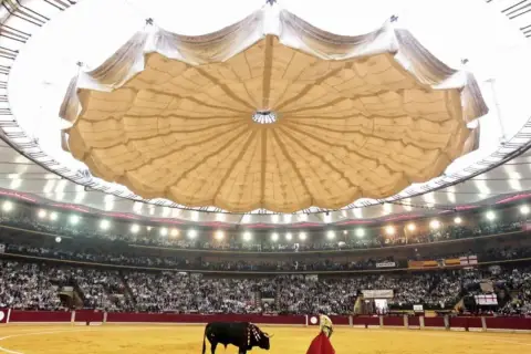 Un torero y un toro en la arena de la plaza de toros La Misericordia, con el público en las gradas y un llamativo techo desplegable.