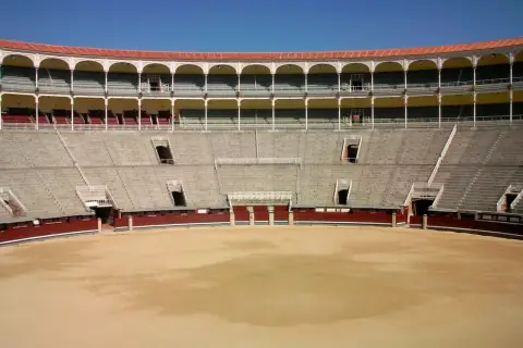 Vista interior de una plaza de toros vacía, con gradas de piedra y balcones arqueados. Las ventas por dentro esperan al público.