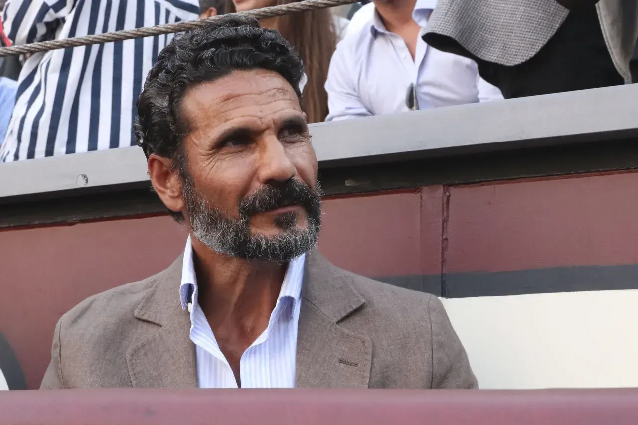 Un torero y actor español, con barba canosa y mirada intensa, viste chaqueta de lino y camisa a rayas.