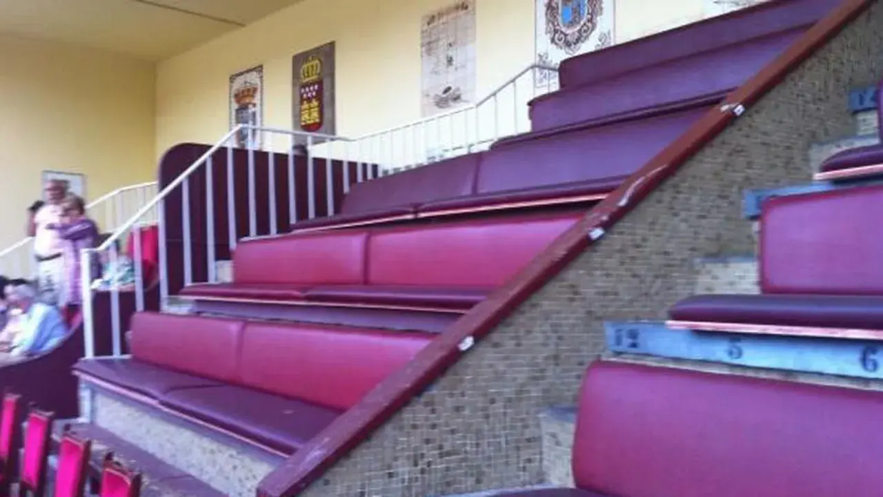 Asientos de terciopelo rojo en un palco de las ventas, con escaleras y barandillas blancas.