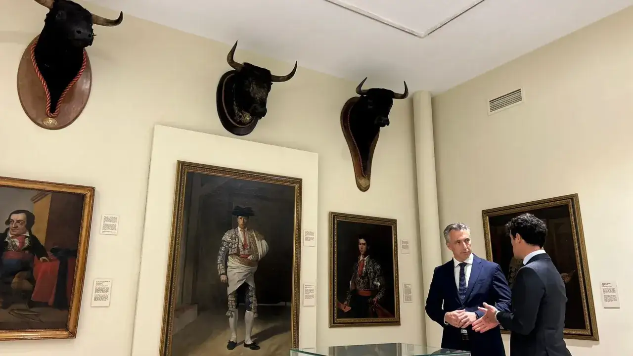 Dos hombres conversan en el museo de las ventas, rodeados de retratos de toreros y cabezas de toro disecadas.