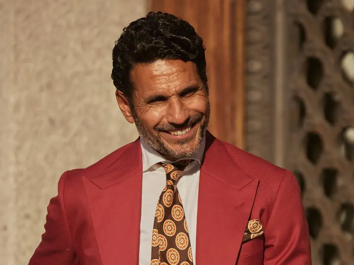 Un sonriente torero y actor espa&ntilde;ol con traje rojo, camisa blanca y corbata estampada.