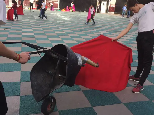 Jóvenes aprenden a torear con un capote y un toro de utilería.