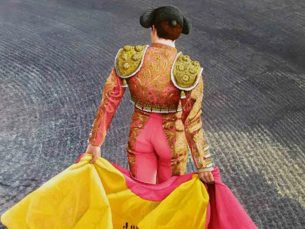 Torero con traje de luces rosa y dorado, sujetando un capote amarillo y rosa. Aprende como hacer un capote de torero.